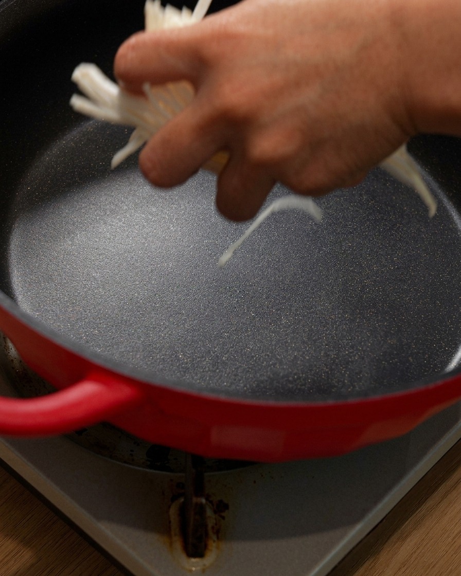 Shredded onions being added into the bottom of a red pot.