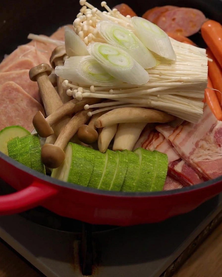 Freshly sliced green onion pieces being placed on top of the ingredients inside the hot pot.