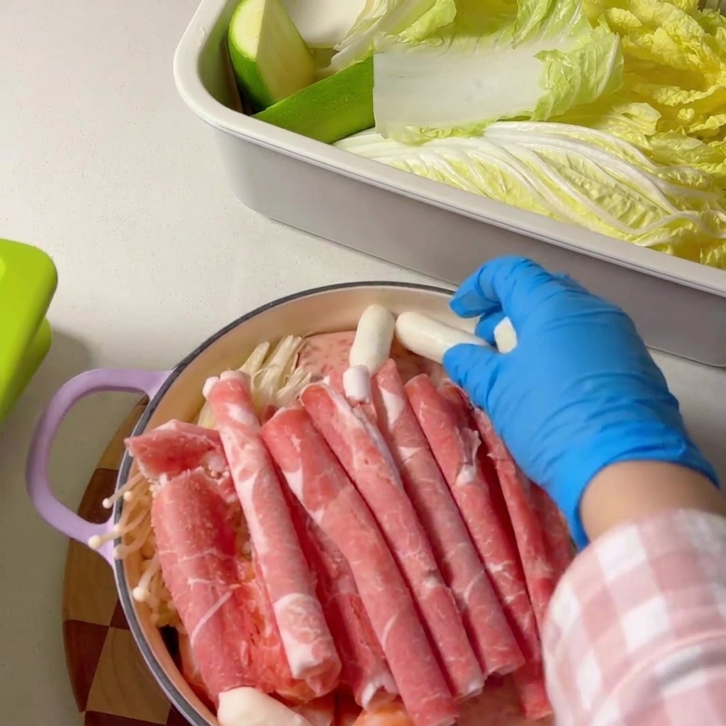 Cheese rice cakes being placed along the edge of the ingredients in the pot.