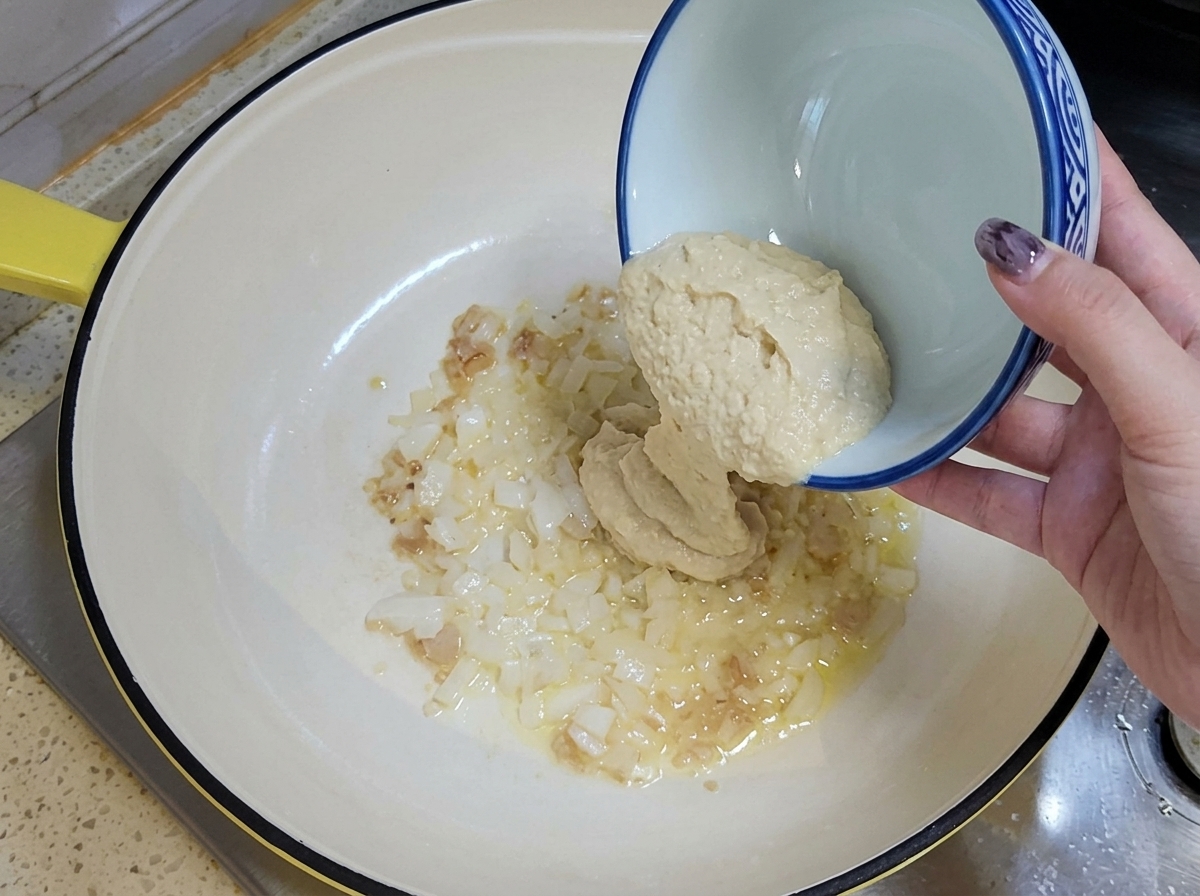 Minced garlic and diced onions being poured into an oiled pan with a ceramic bowl.