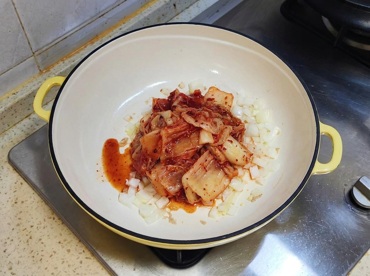 A portion of red fermented kimchi sitting on top of sautéed onions in a white pan.