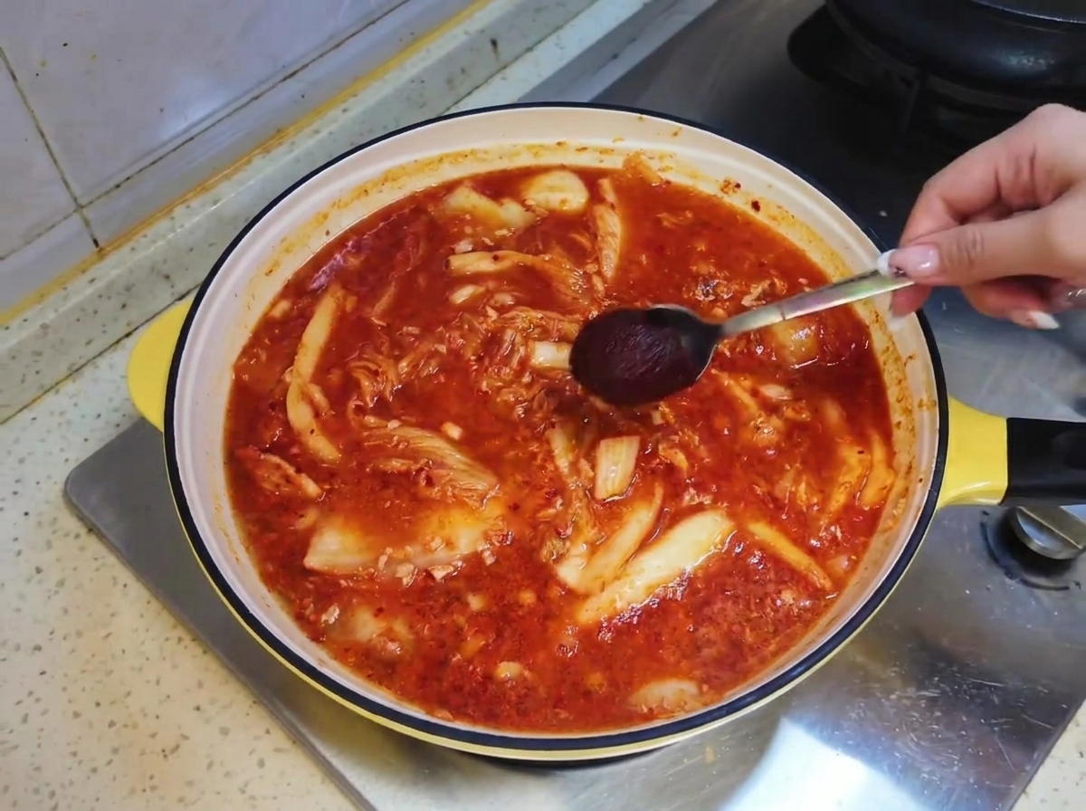 A spoonful of Korean hot sauce being lowered into the reddish soup broth inside the pan.