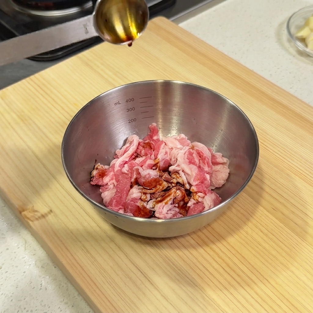 Soy sauce being poured from a measuring spoon into a steel bowl filled with raw beef slices.