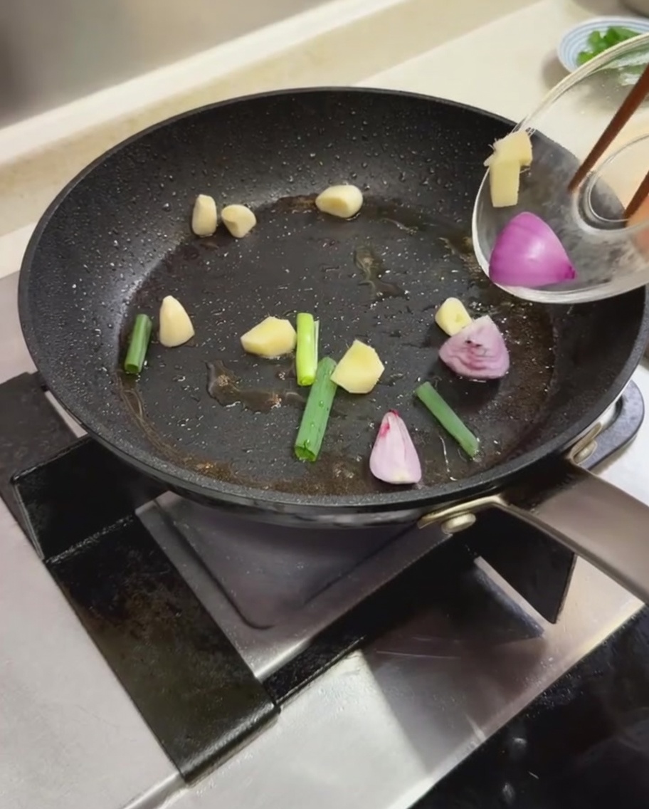 Scallion pieces, garlic cloves, and sliced red onions being sautéed in a hot frying pan.