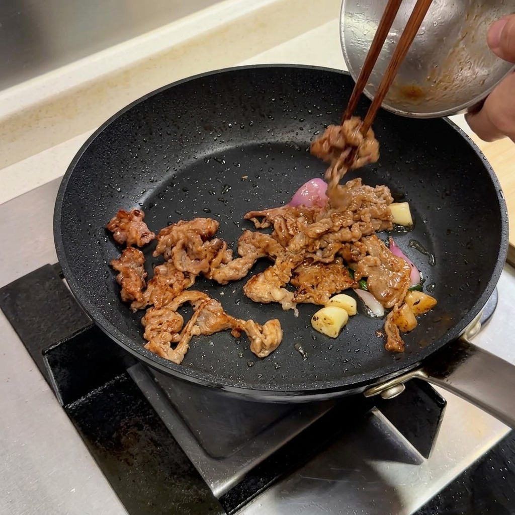 Beef slices and aromatics in a skillet with a pat of butter being added.