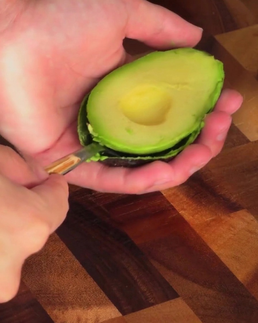 A person using a spoon to scoop the green flesh out of an avocado half.