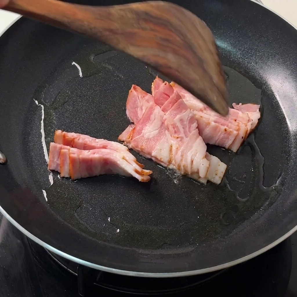 Bacon strips frying in a hot black skillet with a wooden spatula turning them.