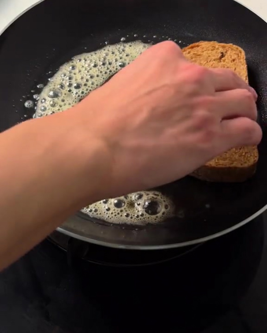 A hand placing a slice of brown bread onto bubbling, melted butter in a hot skillet.