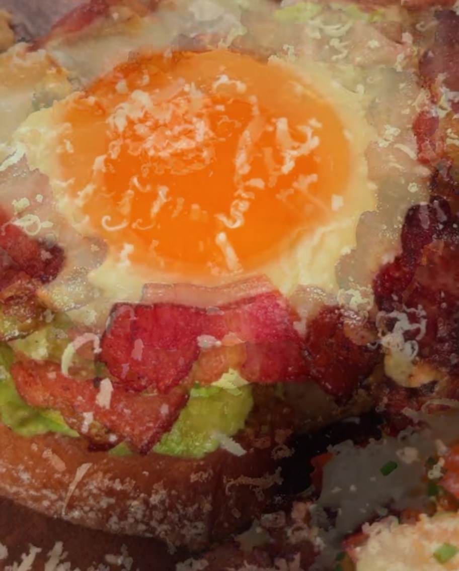Grated Parmesan cheese being sprinkled over the top of a completed avocado and egg sandwich.