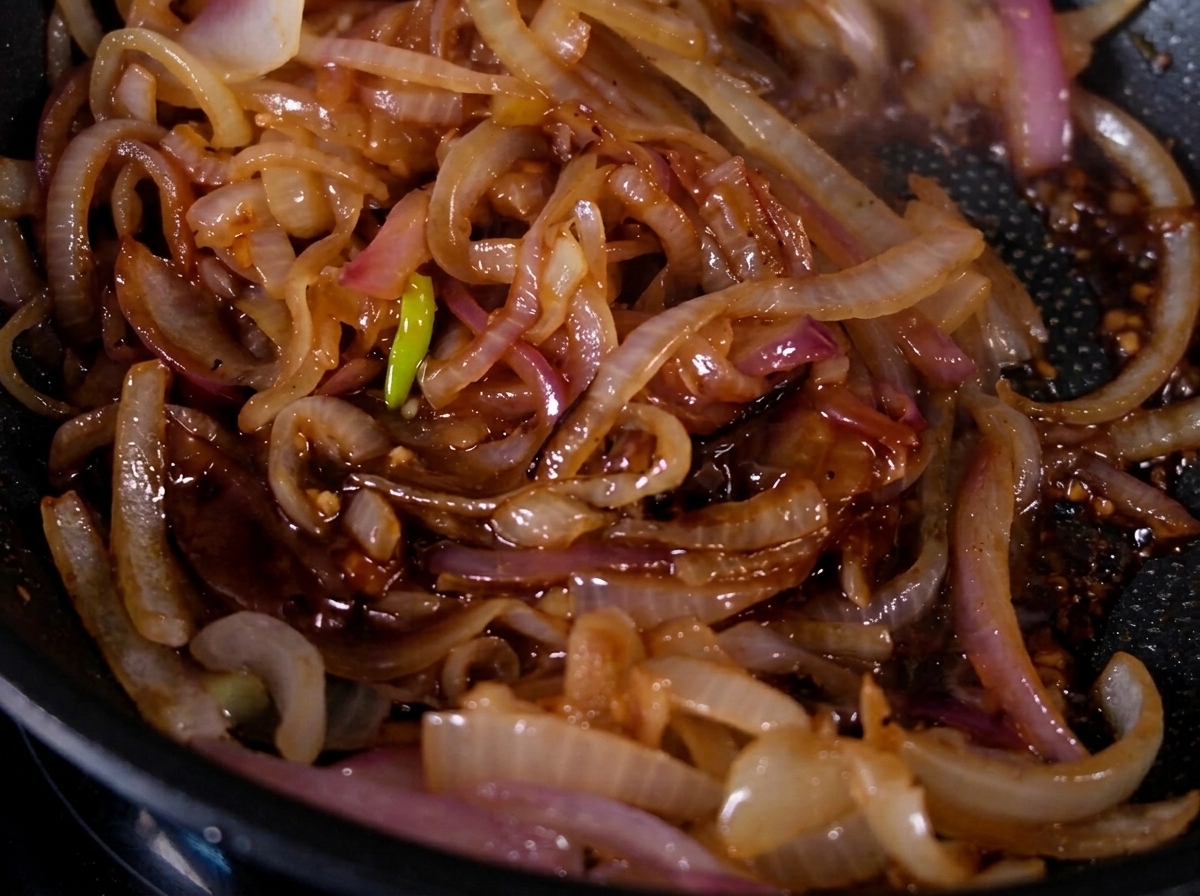 Caramelized onions shimmering with a glossy glaze inside a frying pan.
