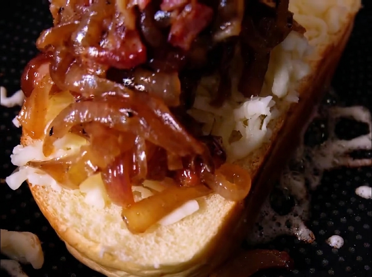 A generous pile of caramelized onions and bacon pieces sitting on top of shredded cheese on a slice of bread.