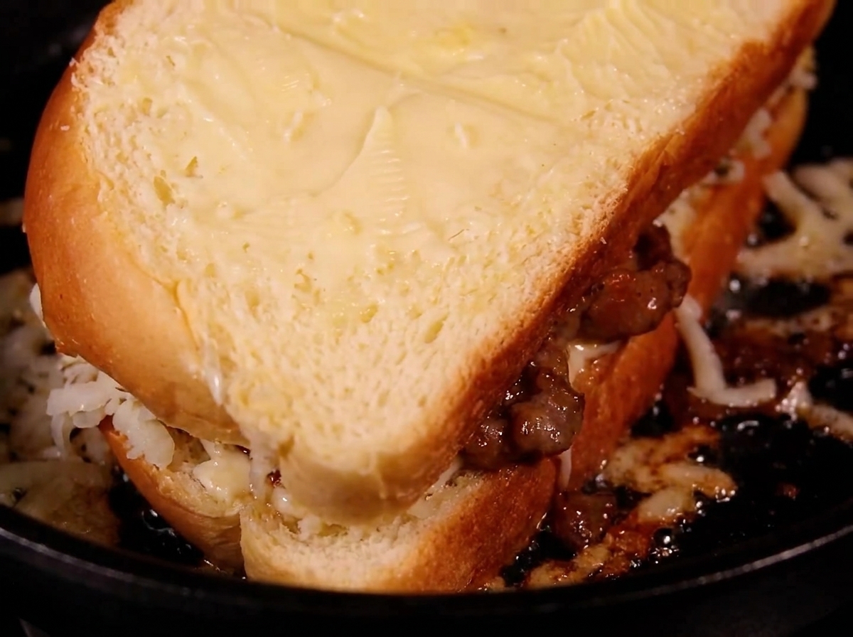 A golden-toasted sandwich being flipped over in a frying pan.