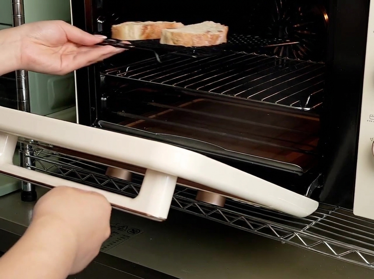 Hands sliding a wire rack holding two slices of bread into a small countertop oven.