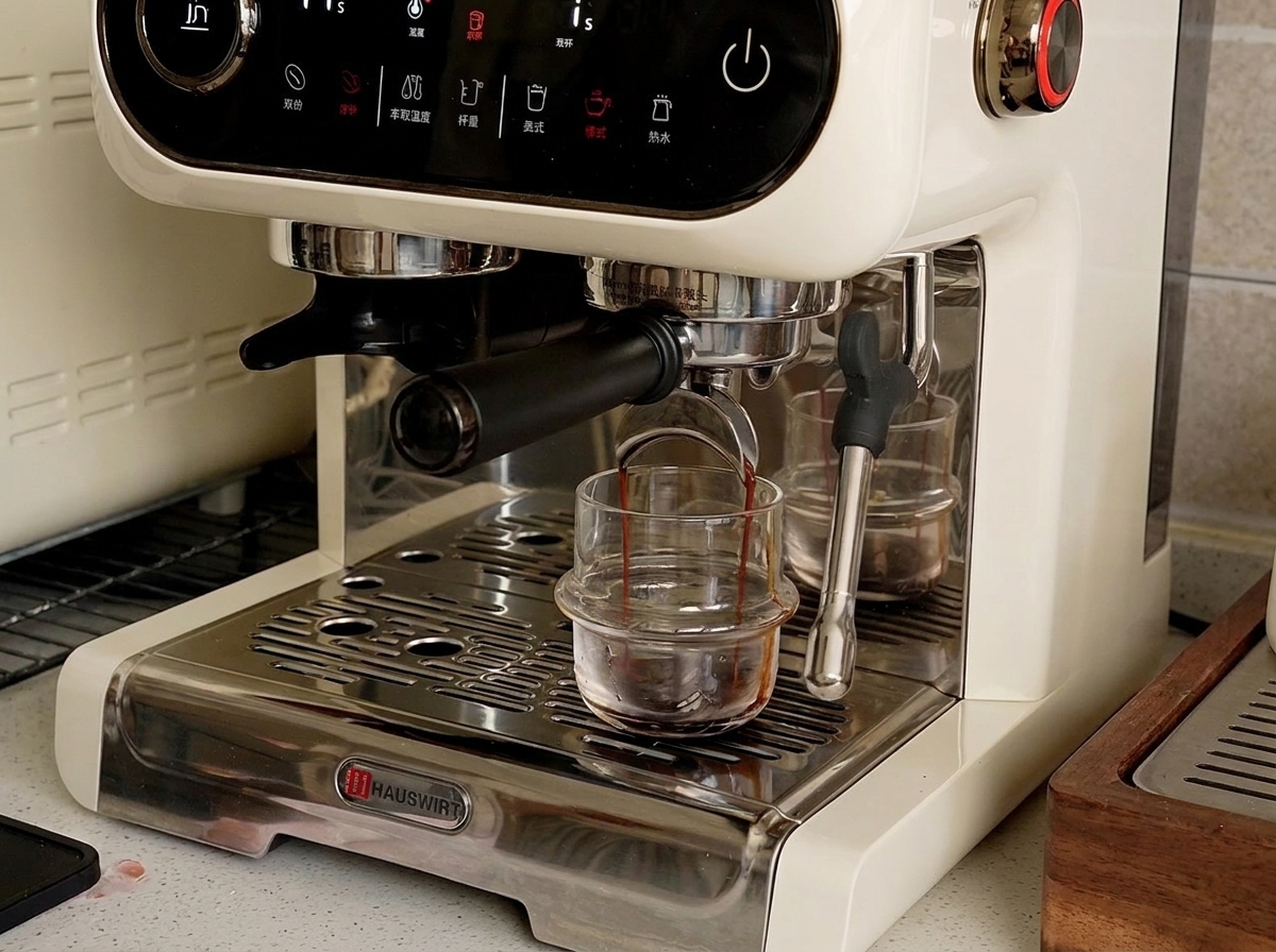 An espresso machine dispensing dark liquid espresso into a small glass cup on the drip tray.