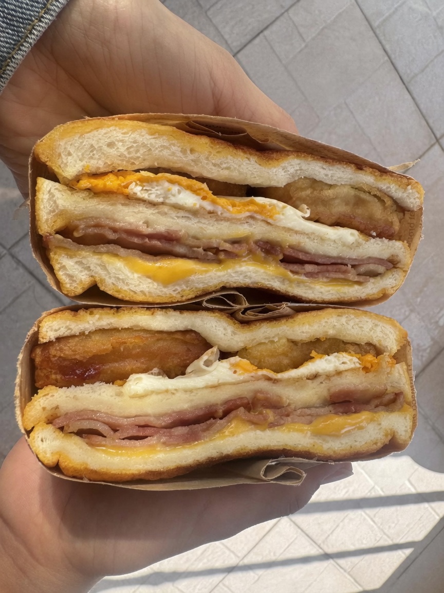 Two halves of the golden-brown air-fried sandwich, revealing layers of chicken nuggets, bacon, fried egg, and melted cheese.