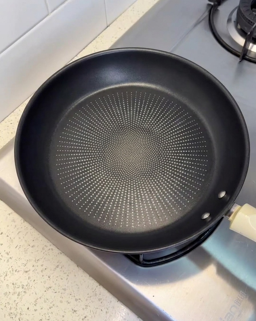 A black non-stick frying pan resting on a stovetop burner, lightly coated with oil.