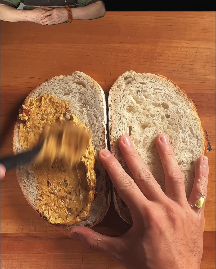 Slices of rustic sourdough bread with a rich spread being smoothed out by a spoon.