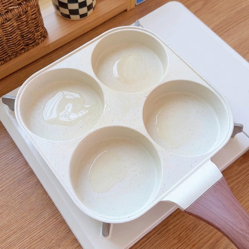 Eggs being poured into the oiled compartments of a multi-cup frying pan.