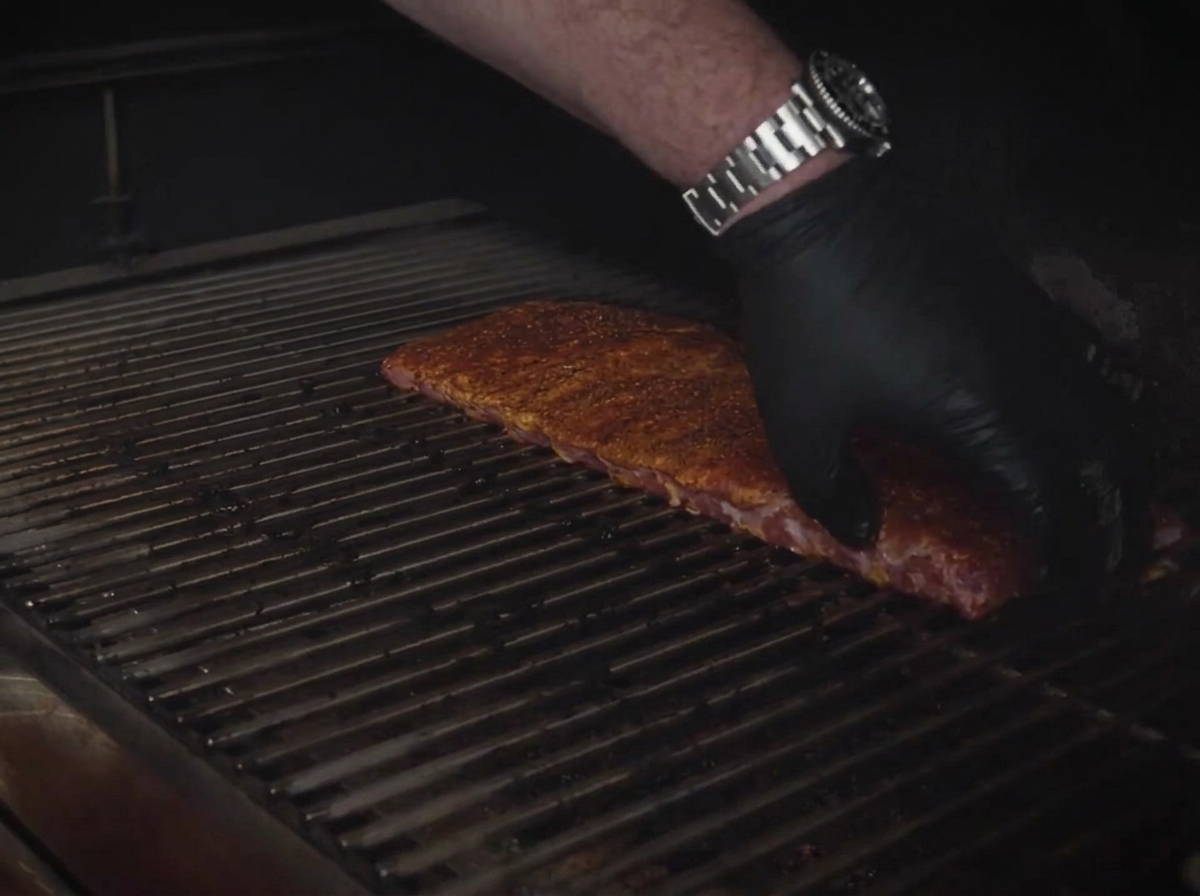 Seasoned St. Louis ribs being laid out flat onto the metal cooking grates of a smoker.