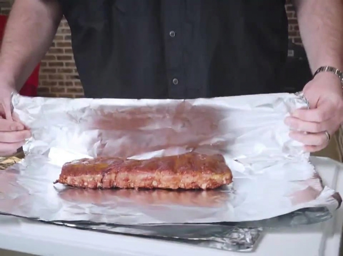Smoked ribs placed on a sheet of aluminum foil, ready to be wrapped tightly bone side down.
