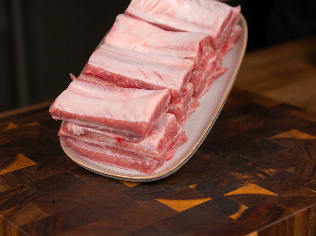 Fresh, raw pork ribs neatly stacked on an oval white plate, resting on a wooden cutting board.