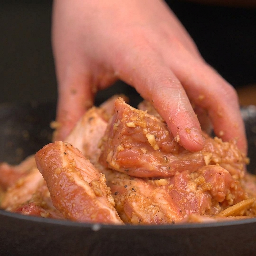 A hand actively mixing raw pork ribs with a thick, savory, garlic-rich marinade in a bowl.