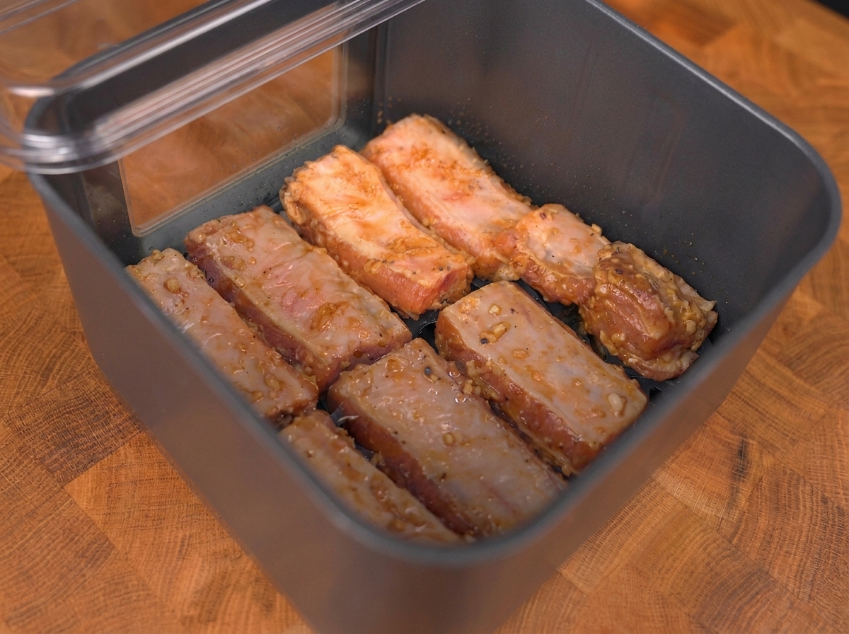Marinated pork ribs arranged in a single layer inside the air fryer basket.