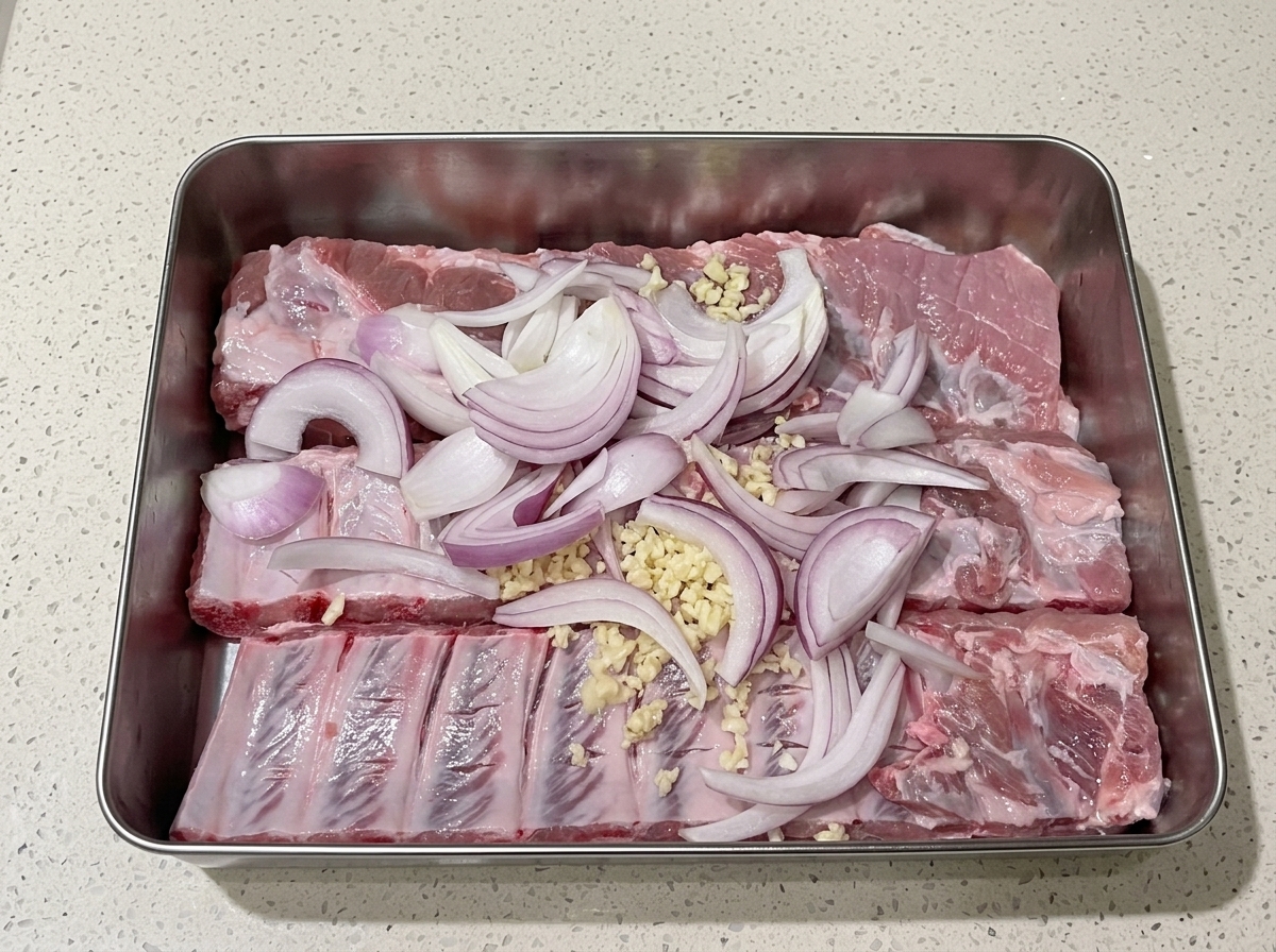 Sliced red onions distributed over the pork ribs as juice is applied.