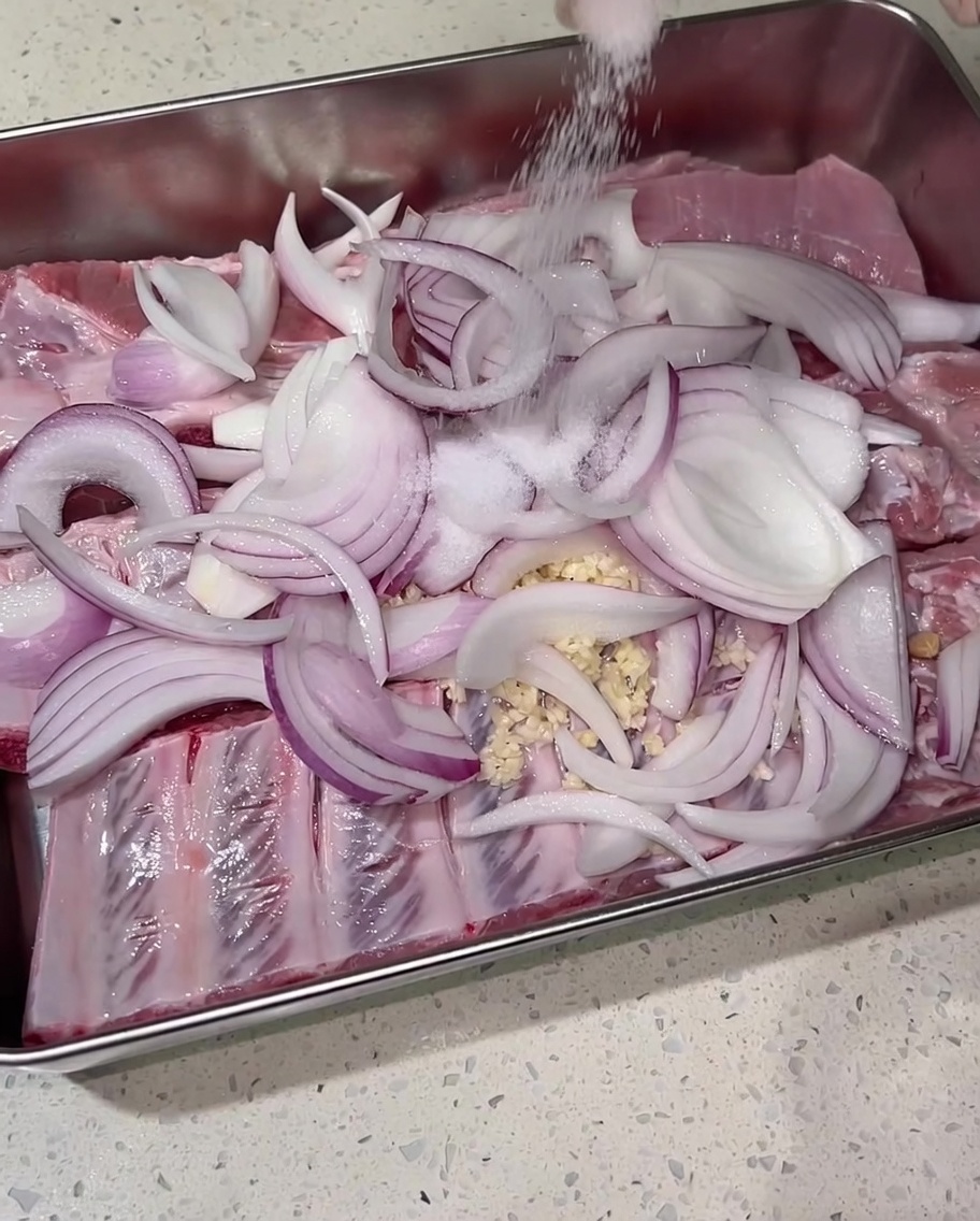 Salt being hand-sprinkled generously over the seasoned pork ribs and onions.