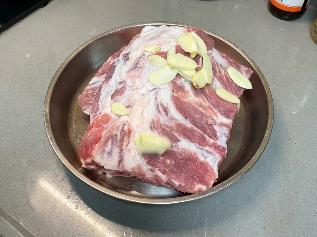 Garlic slices scattered evenly over raw pork ribs resting in a metal tray.
