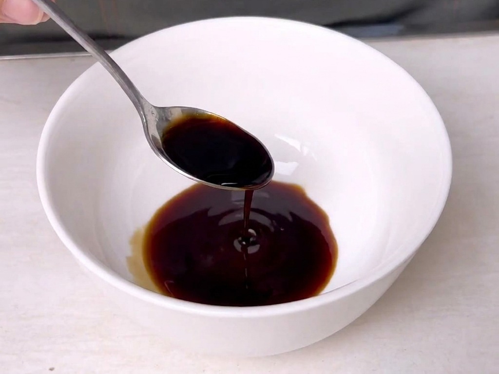 A metal spoon stirring a dark, rich sauce inside a small white ceramic bowl.