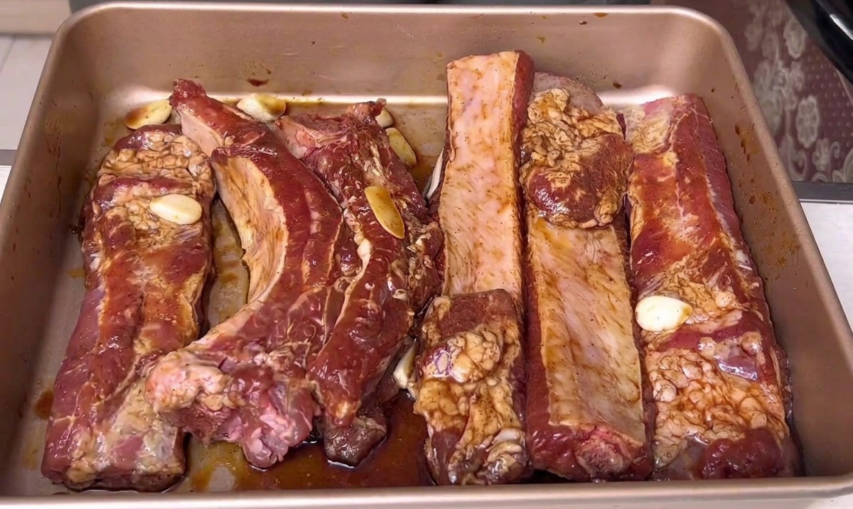 Marinated pork ribs resting in a golden baking tray, ready to be placed into the oven.
