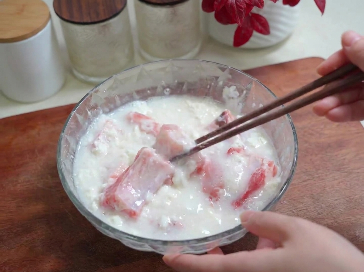 Water being poured into a glass bowl of ribs, salt, and flour while being mixed with chopsticks.
