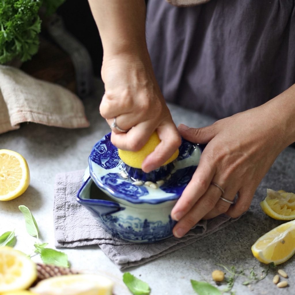 Hands pressing and twisting a lemon half over a blue and white ceramic manual juicer.