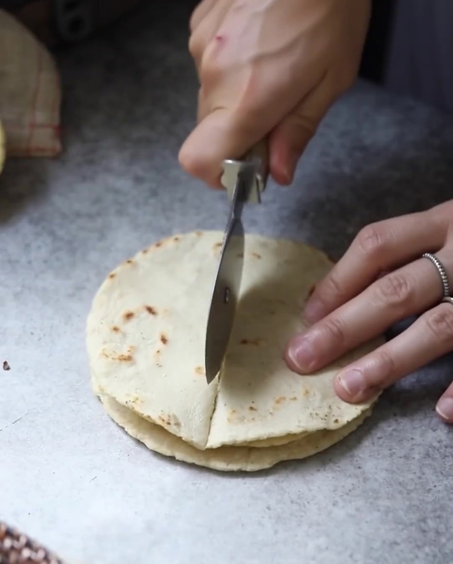 Stacked cooked tortilla flatbreads being cut into triangular sections with a blade.