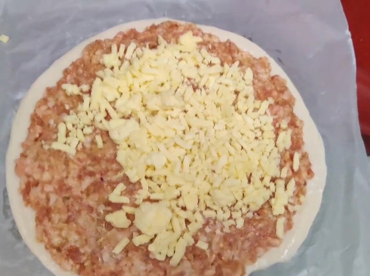 Shredded yellow cheese piled on top of a layer of raw minced meat on a scallion pancake.
