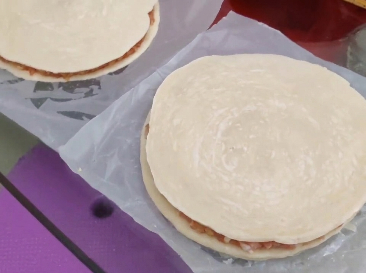 A second round scallion pancake being placed over the meat and cheese filling to form a closed pie.