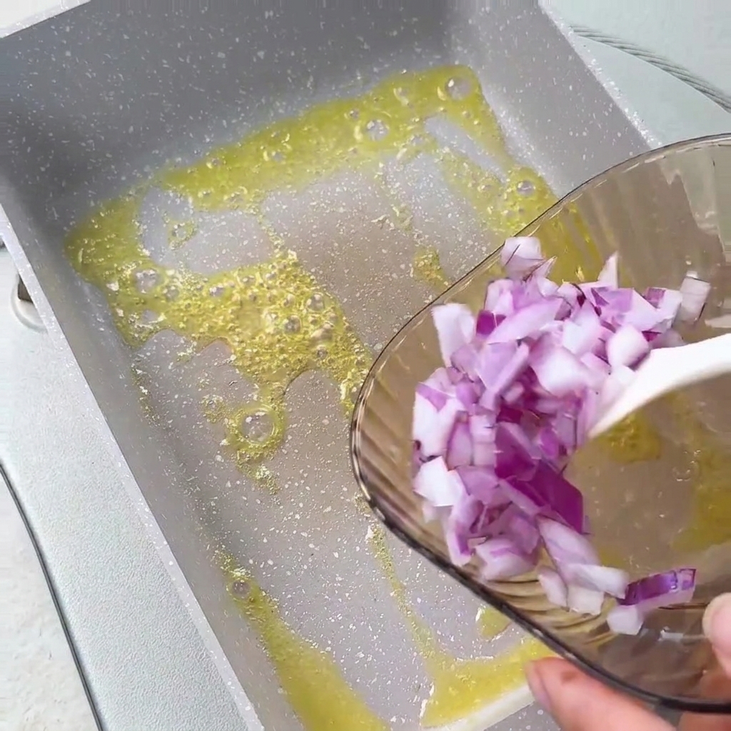 Chopped red onions being poured from a glass bowl into melted butter in a square pan.