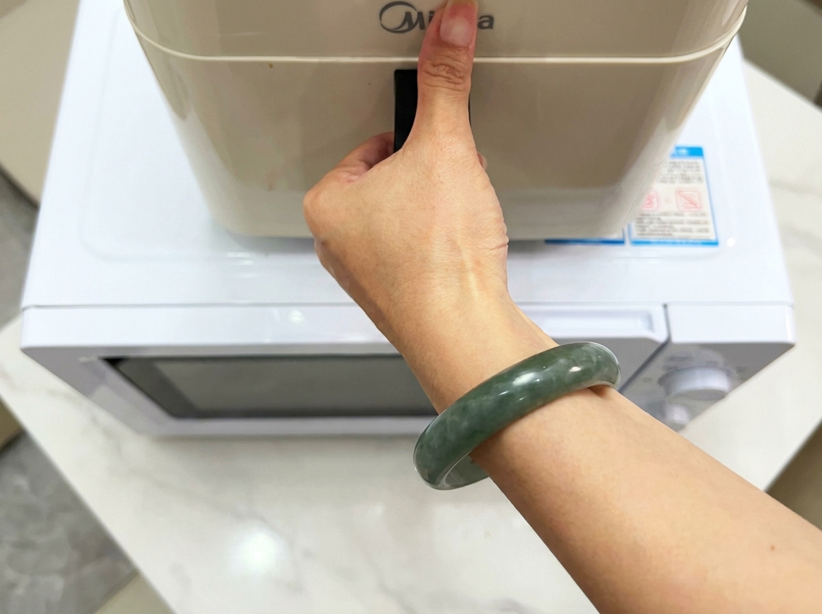 A hand holding the handle of a modern kitchen appliance sitting on a white surface.