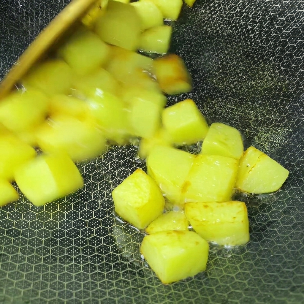 Potato cubes frying in oil inside a wok until golden brown.