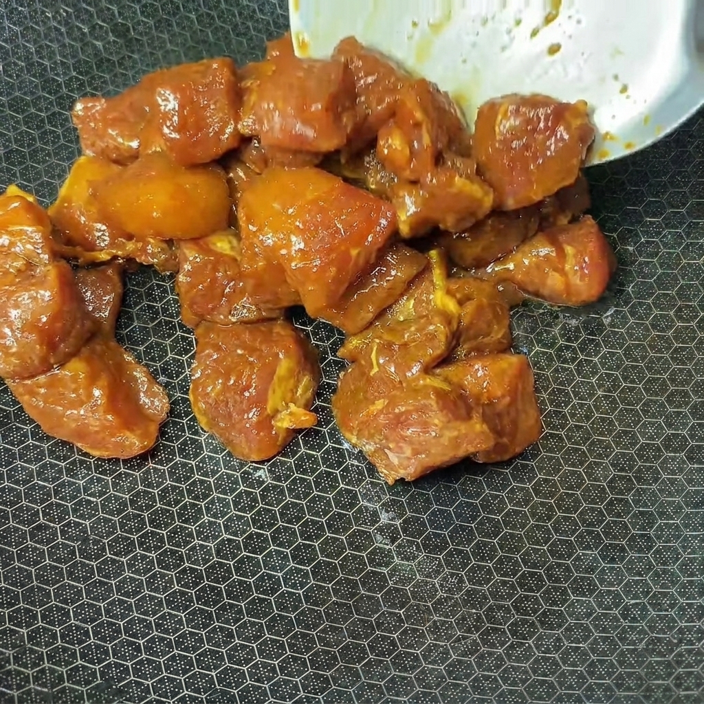 Marinated pork cubes being placed into a hot wok for cooking.