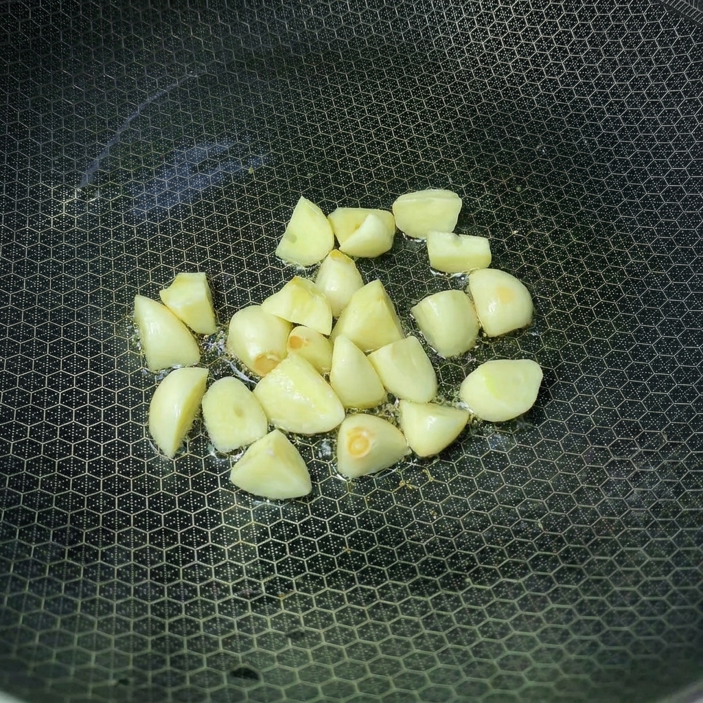 Garlic cloves frying in a wok with hot oil.