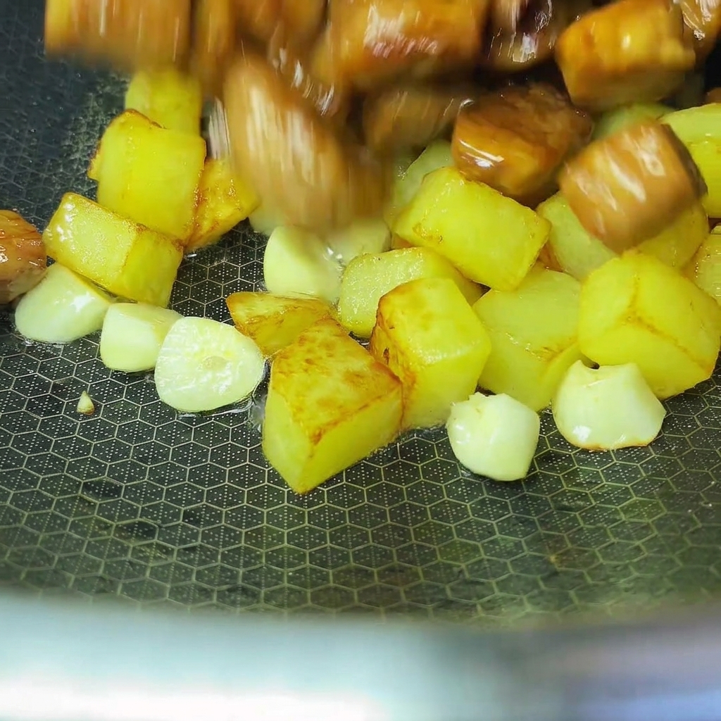 Cooked potatoes and pork being combined together in a wok.
