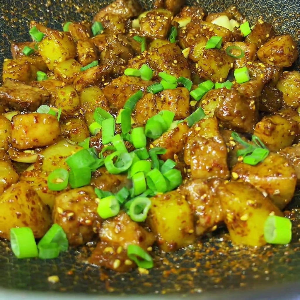 Freshly chopped green onions sprinkled over the finished barbecue cumin pork and potatoes in a wok.
