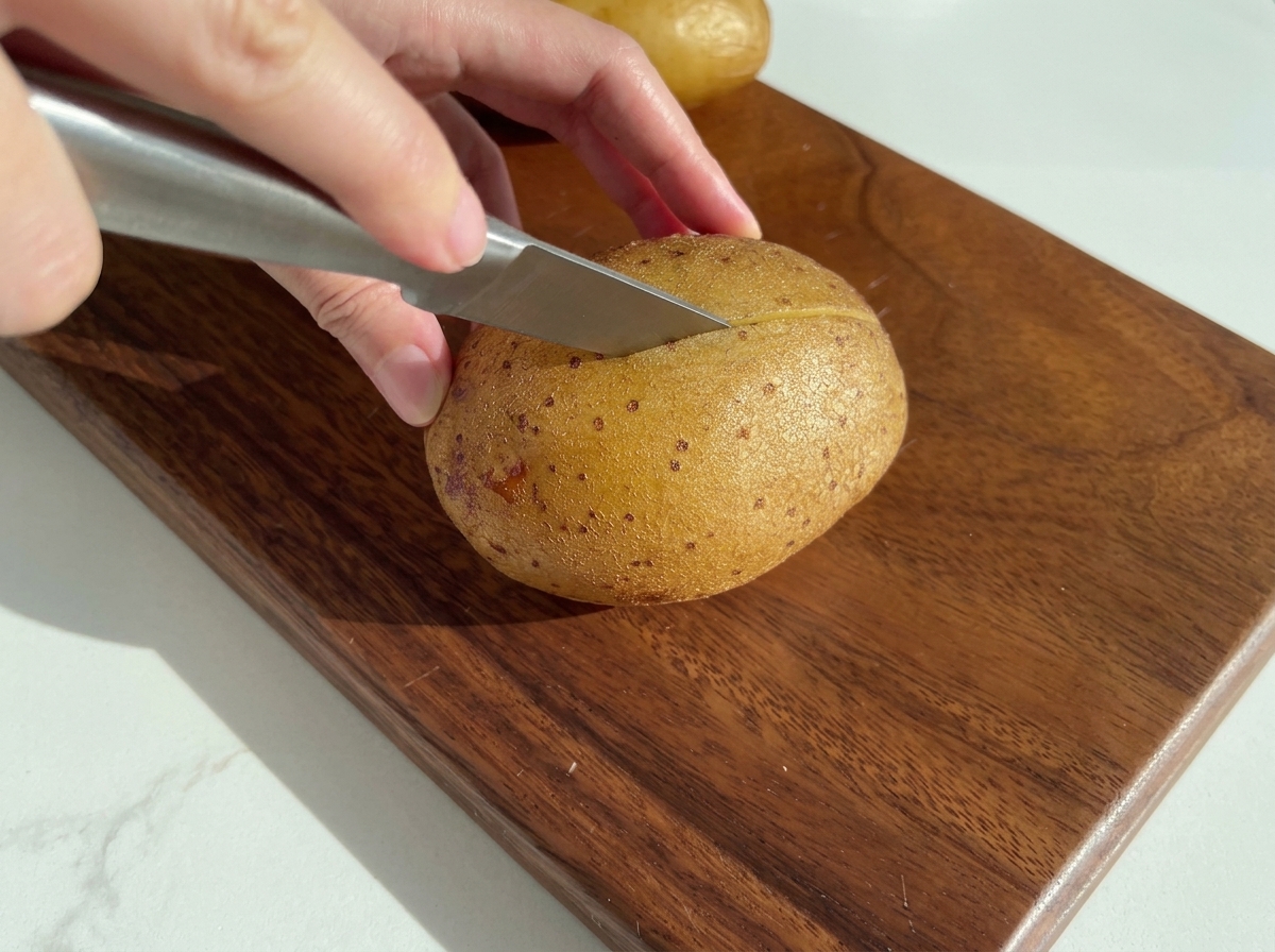 A knife slicing through a baked potato on a wooden board.