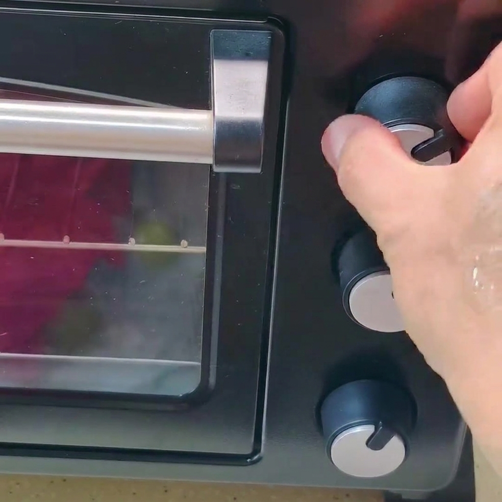A hand turning the temperature control knob on a black oven.