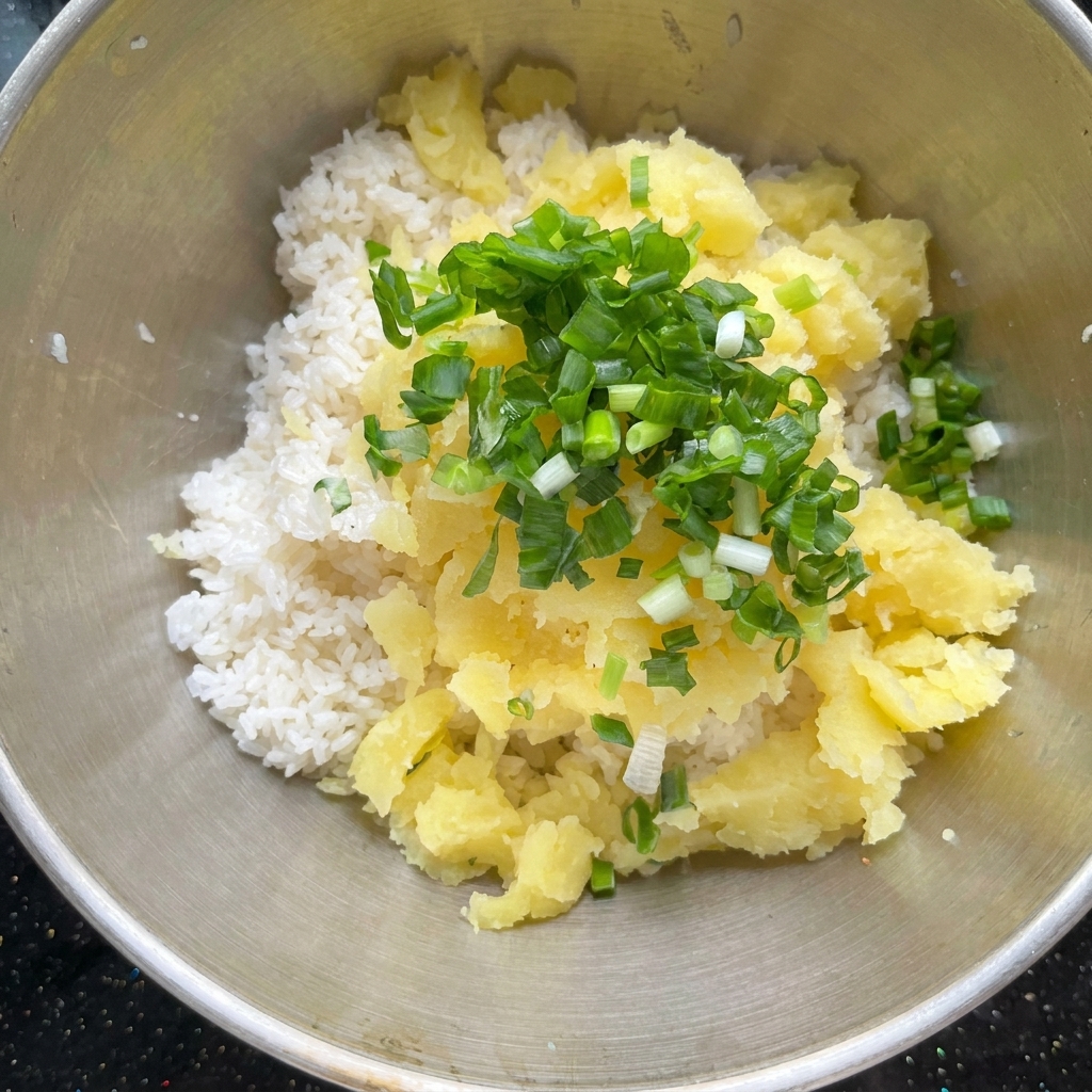 Baked potato pieces and seasonings being combined with cooked rice in a metal bowl.