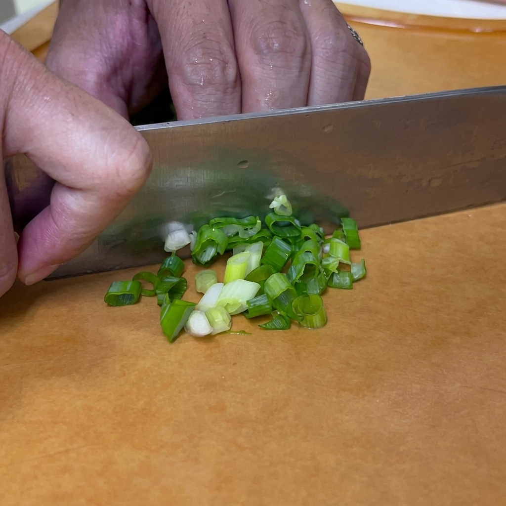 Green onions being chopped into small round pieces with a knife on a cutting board.