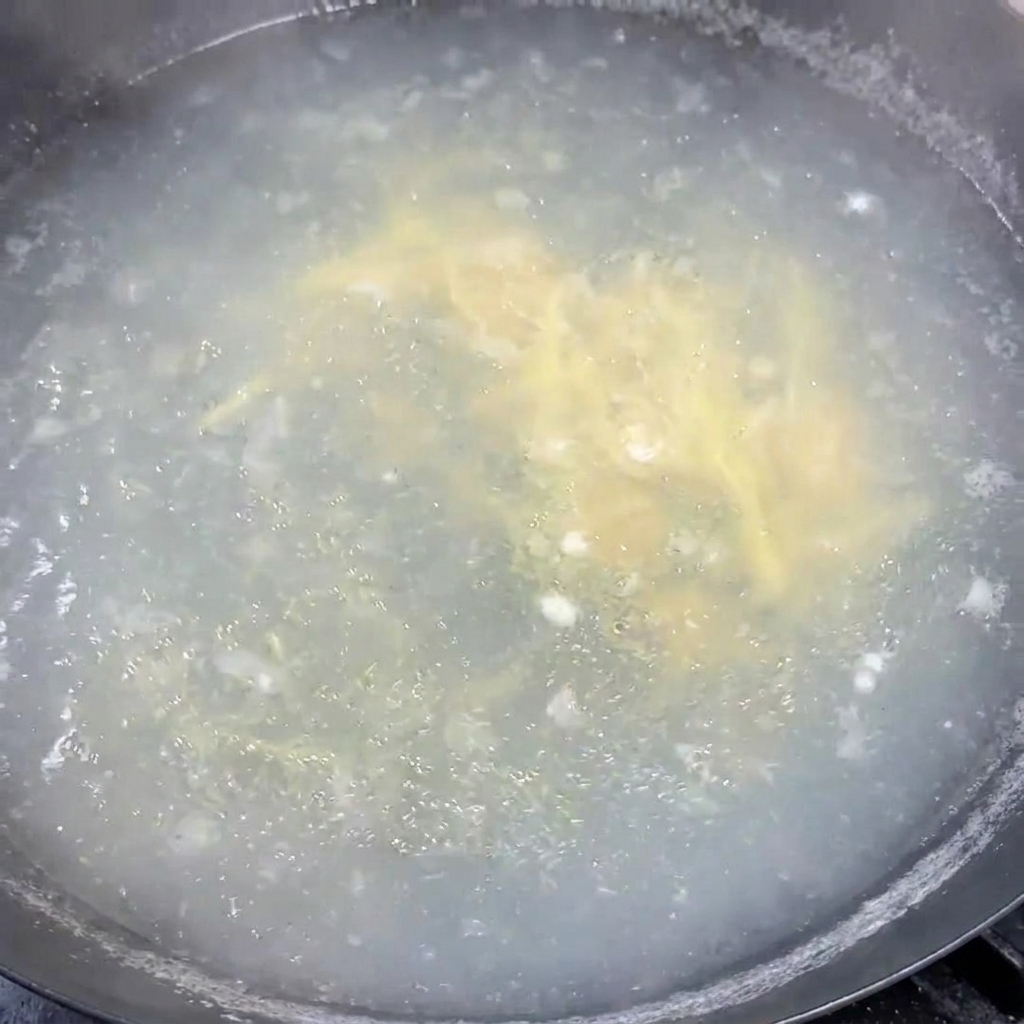 Chopped green onions being stirred evenly into a pot of hot simmering soup.