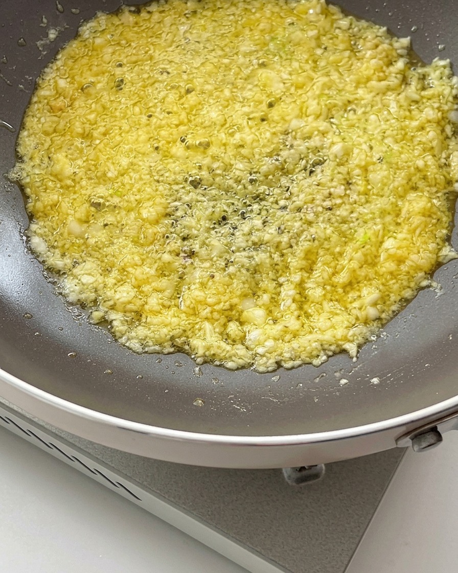 Soy sauce and oyster sauce being poured into the sizzling garlic butter mixture in a frying pan.